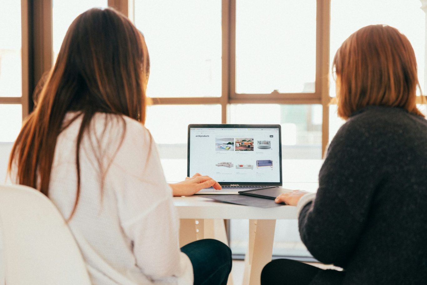 Zwei Personen sitzen an einem Tisch und arbeiten zusammen an einem Laptop.